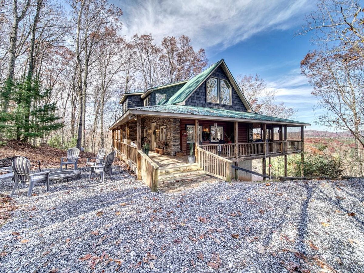Classic mountain retreat with stairs leading up to a wide two-story porch surrounded by trees. Relax in the hot tub or grab a seat by the fire pit—it’s the peaceful break you’ve been needing.