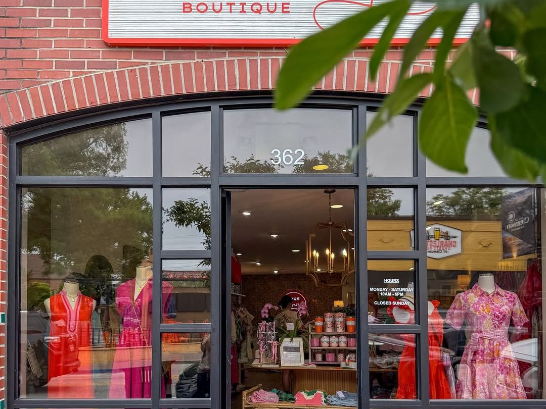 A boutique storefront with bold, colorful dresses on display invites shoppers to explore. This cozy shop blends fashion and charm right in the heart of downtown.