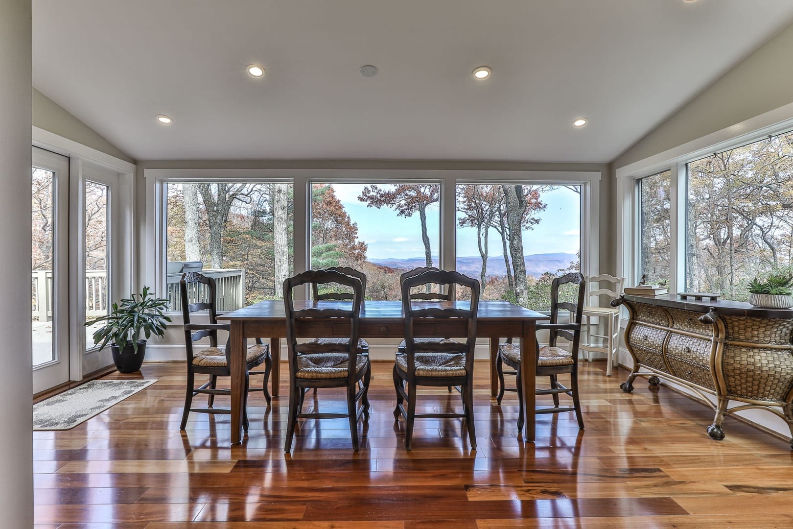 Dining room with a wooden table and six chairs set against large windows showcasing a mountain and forest view.