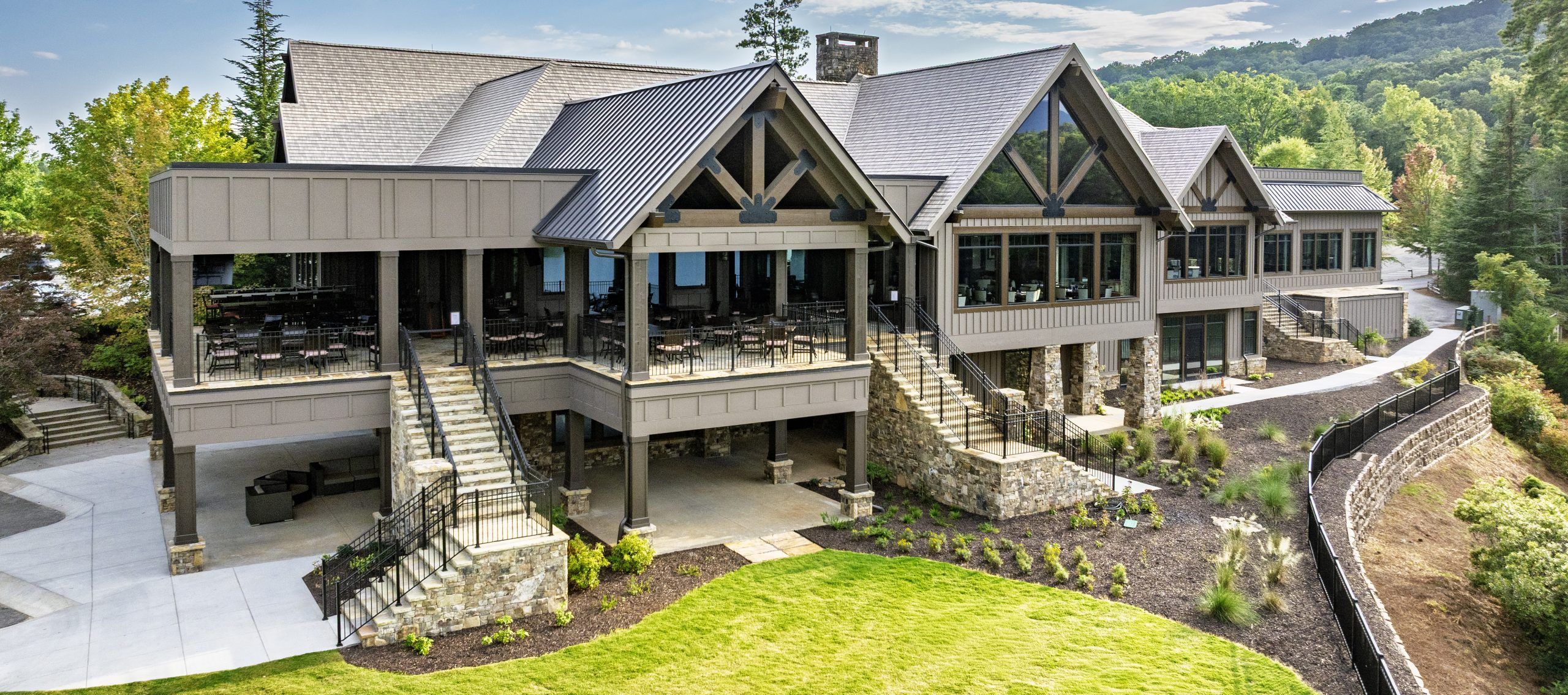 The Big Canoe Clubhouse in Georgia features a striking mountain lodge design with stone accents, large windows, and multiple terraces for dining and events. Surrounded by greenery and mountain views, it offers an inviting mix of elegance and rustic charm.
