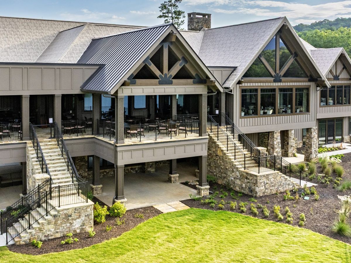 The Big Canoe Clubhouse in Georgia features a striking mountain lodge design with stone accents, large windows, and multiple terraces for dining and events. Surrounded by greenery and mountain views, it offers an inviting mix of elegance and rustic charm.