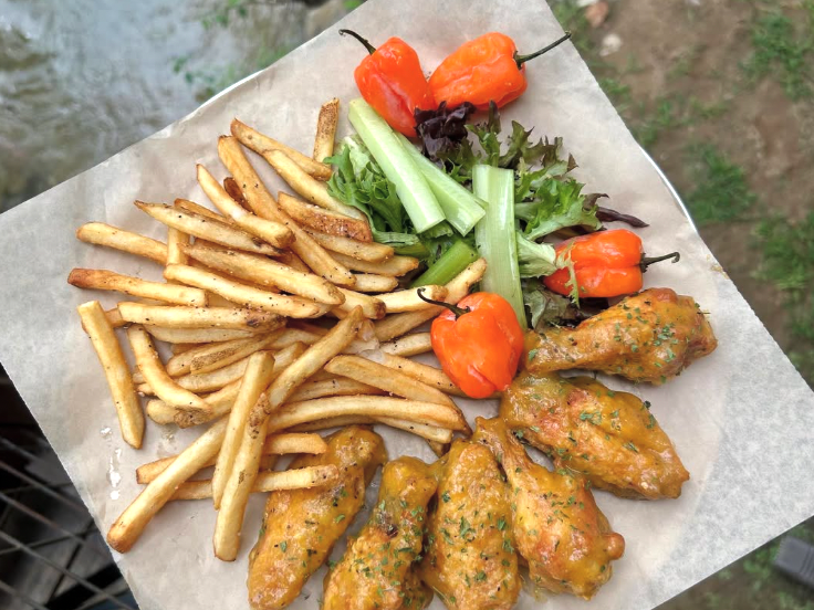 A platter of golden fries, saucy chicken wings, fresh celery with greens, and bright orange peppers served on parchment paper.