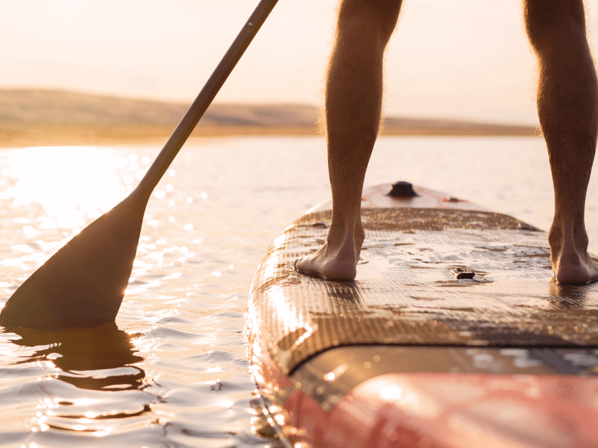 A paddleboarder stands steady on calm golden waters as the sun begins to set. Stand-up paddleboarding at Kiawah Island is a mix of balance, peace, and scenic views you won’t forget.