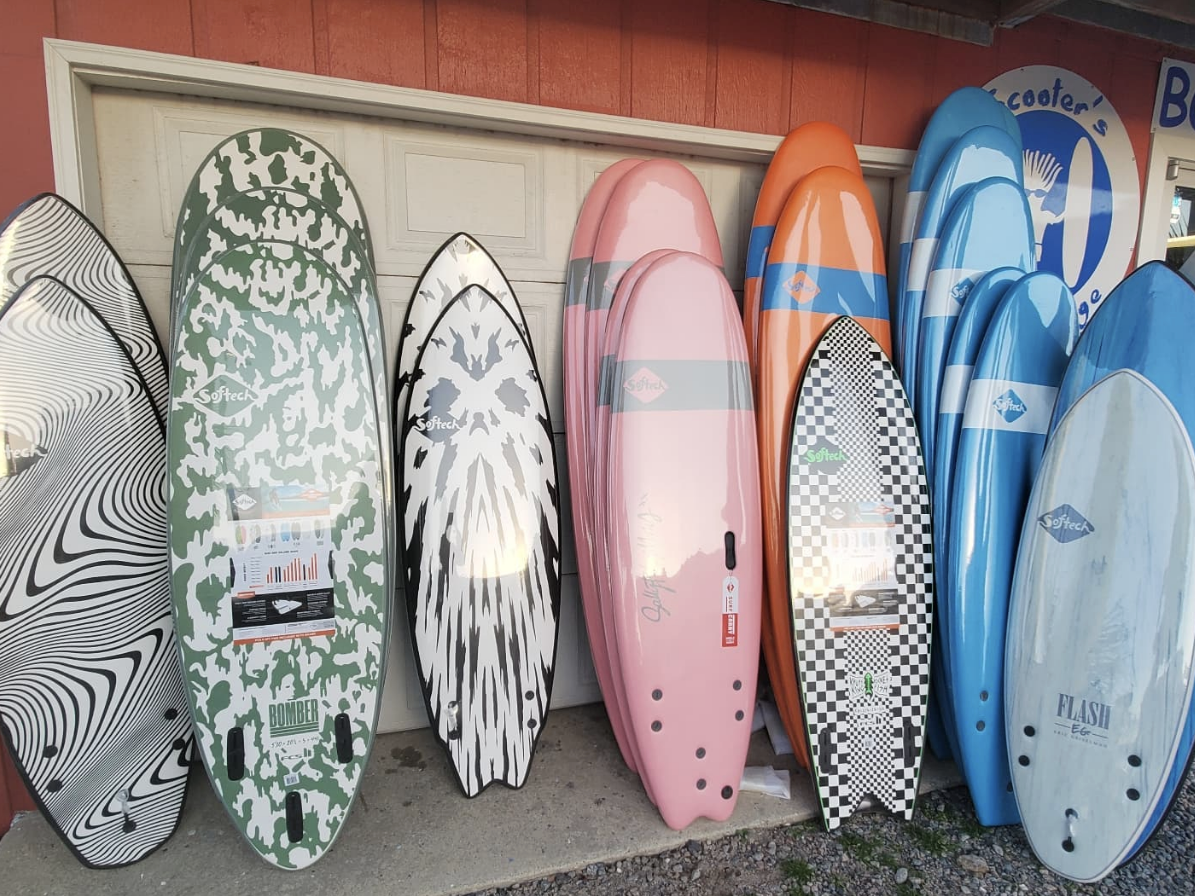 A colorful lineup of Softech surfboards in various sizes and patterns, leaning against a building outside a surf shop.