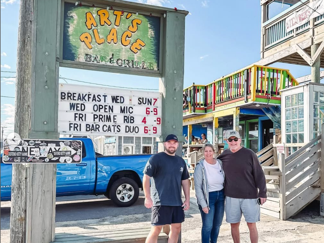 3 people standing side by side with sign on the back painted arts place