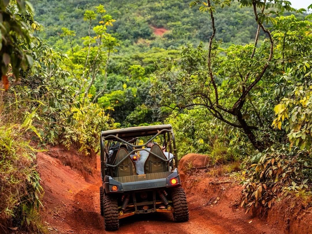 An off-road UTV navigates a red dirt trail through dense tropical jungle during a Kipu Ranch Adventures guided off-road tour in Kauai, Hawaii.