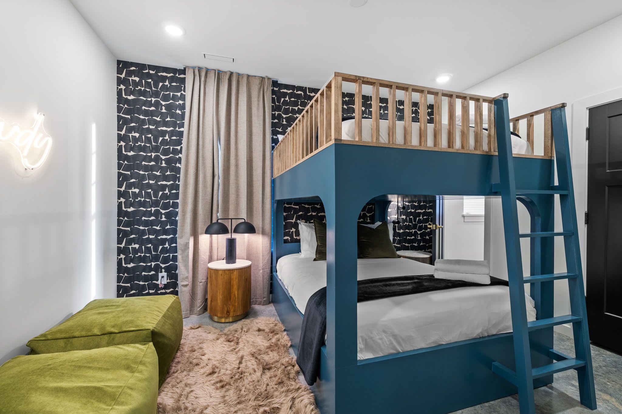 A stylish bunk bedroom featuring a custom teal bunk bed with two sleeping levels, bold patterned wallpaper, soft neutral lighting, and cozy modern accents designed for group stays in Nashville.