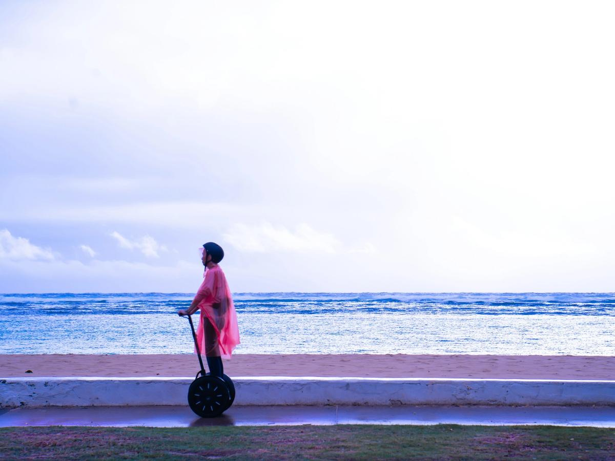 A person rides a Segway along the shore in a pink poncho, with ocean waves rolling in behind them. A chill way to explore Holden Beach.