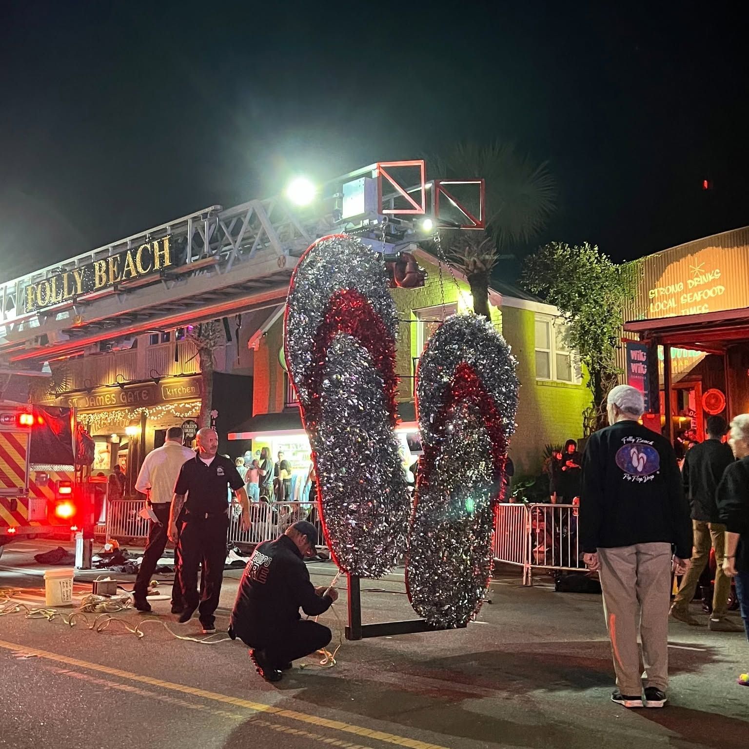 Crews prepare the iconic giant glittering flip flop drop at the Folly Beach New Year's Eve countdown celebration on Center Street, with the Folly Beach fire truck ladder and beachside bars lit up in the background