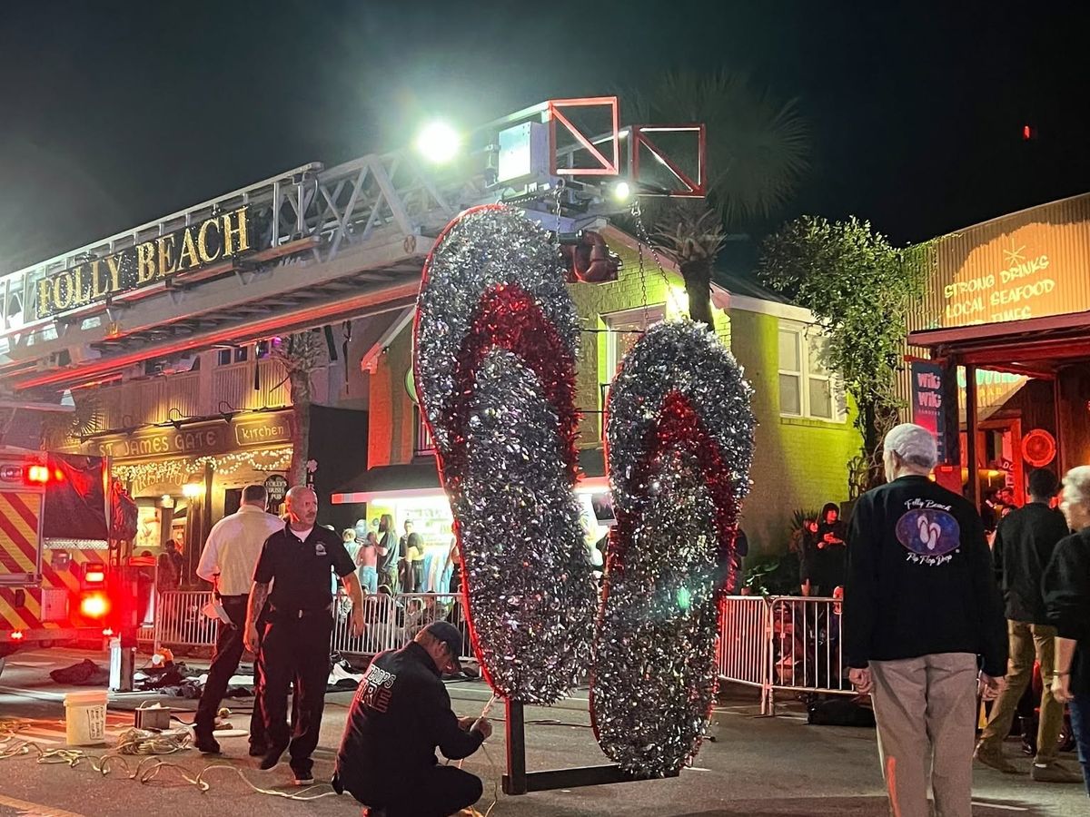 Crews prepare the iconic giant glittering flip flop drop at the Folly Beach New Year's Eve countdown celebration on Center Street, with the Folly Beach fire truck ladder and beachside bars lit up in the background