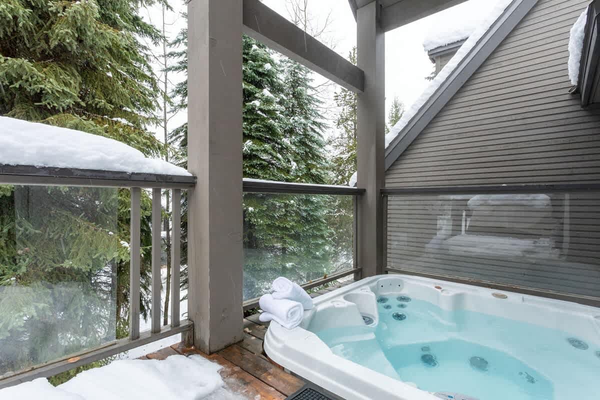 Private balcony hot tub with bubbling jets and neatly folded towels, surrounded by snow-dusted railings and evergreen trees in a peaceful winter setting.