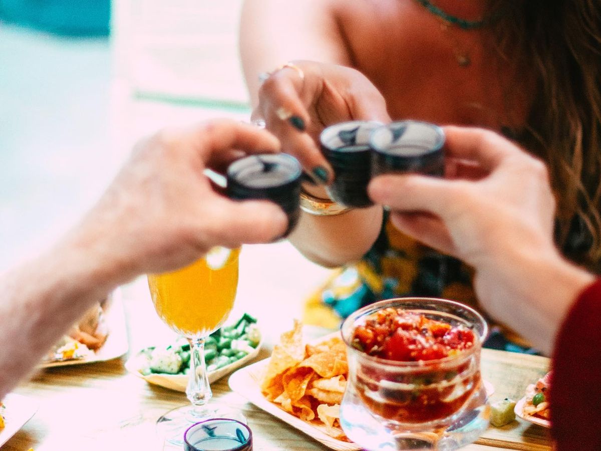 A group of friends toasting over a colorful table full of tacos, dips, and cocktails. A joyful moment of sharing food, drinks, and laughter in a lively atmosphere.