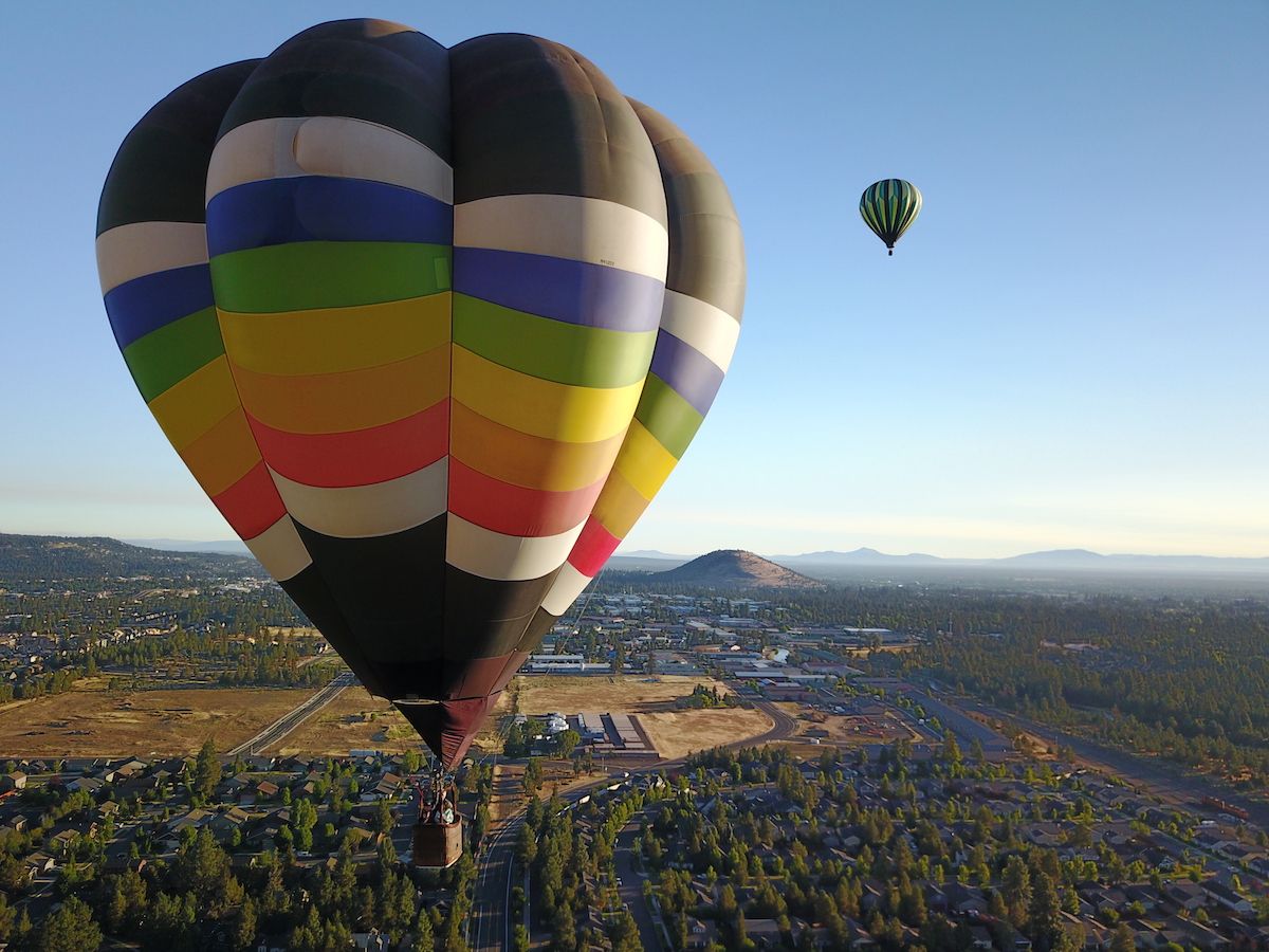 Colorful hot air balloons float gracefully above Bend, Oregon, during sunrise. The bright stripes and mountain backdrop make for a breathtaking view over the city.