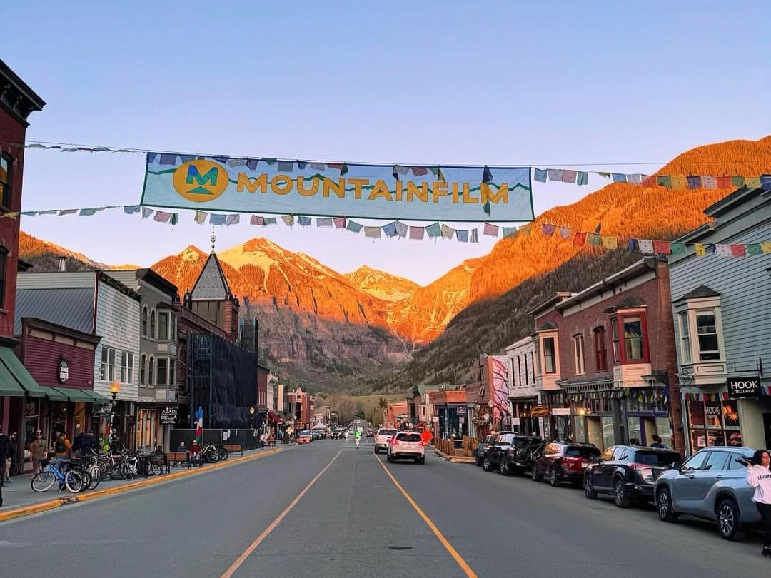 A banner for the Mountainfilm Festival hangs over a quiet Telluride street at sunset, with golden light hitting the mountains. Film lovers gather here every year for documentaries and stories that inspire.