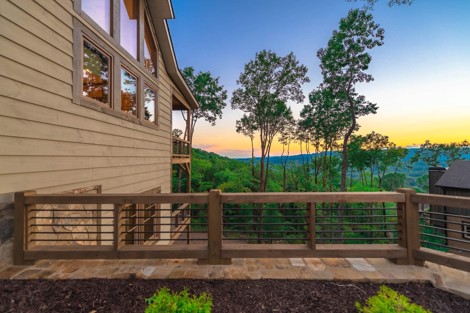 Modern mountain cabin with a wooden deck overlooks a vibrant sunset and tree-covered hills in the Blue Ridge Mountains.
