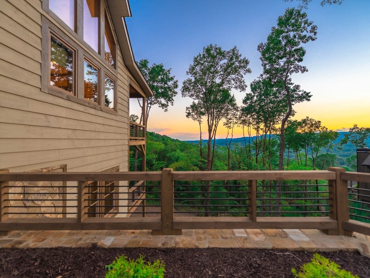 Modern mountain cabin with a wooden deck overlooks a vibrant sunset and tree-covered hills in the Blue Ridge Mountains.