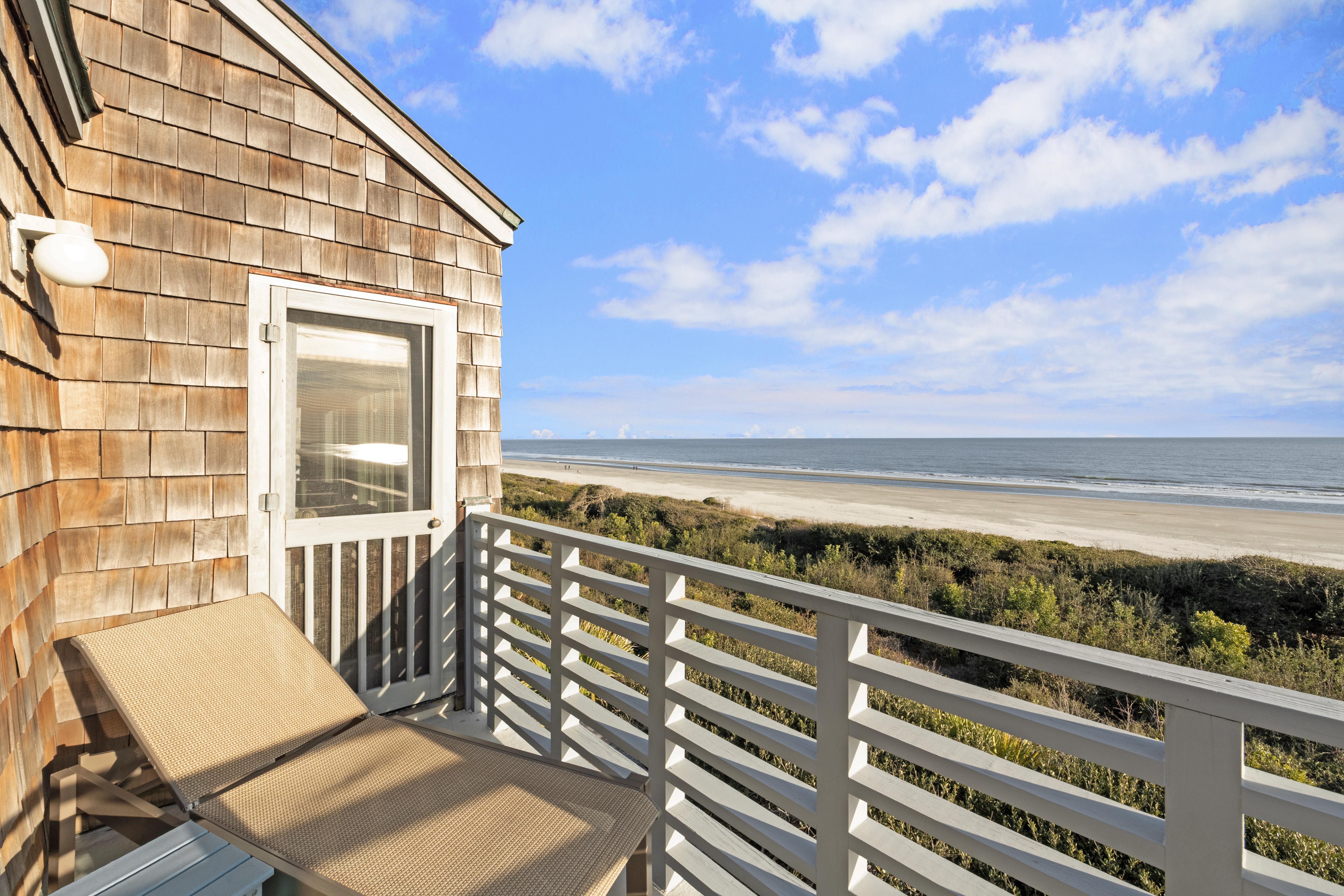tan lounge chair with white balcony rail and beach with ocean waves crashing in sand
