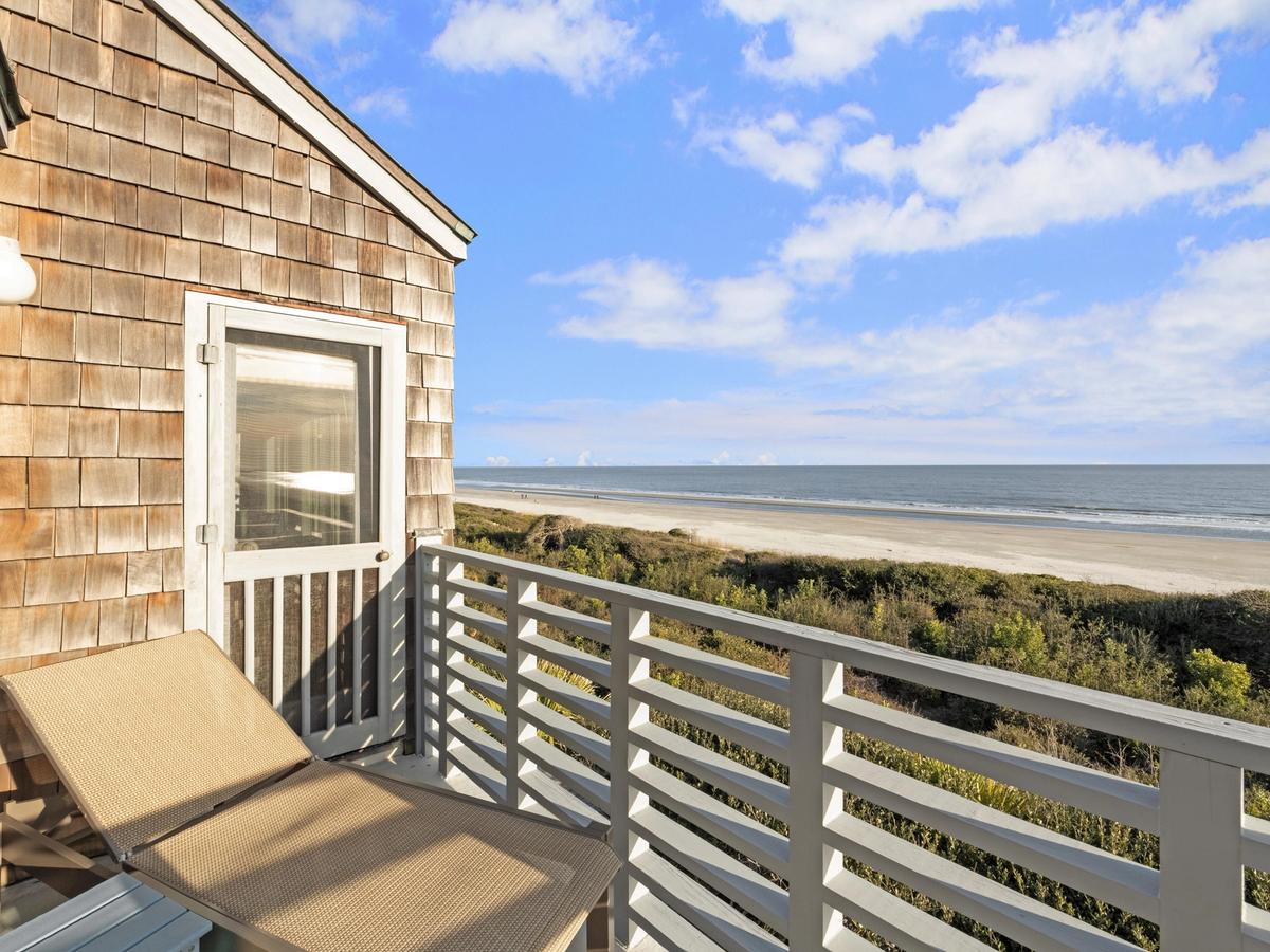 tan lounge chair with white balcony rail and beach with ocean waves crashing in sand