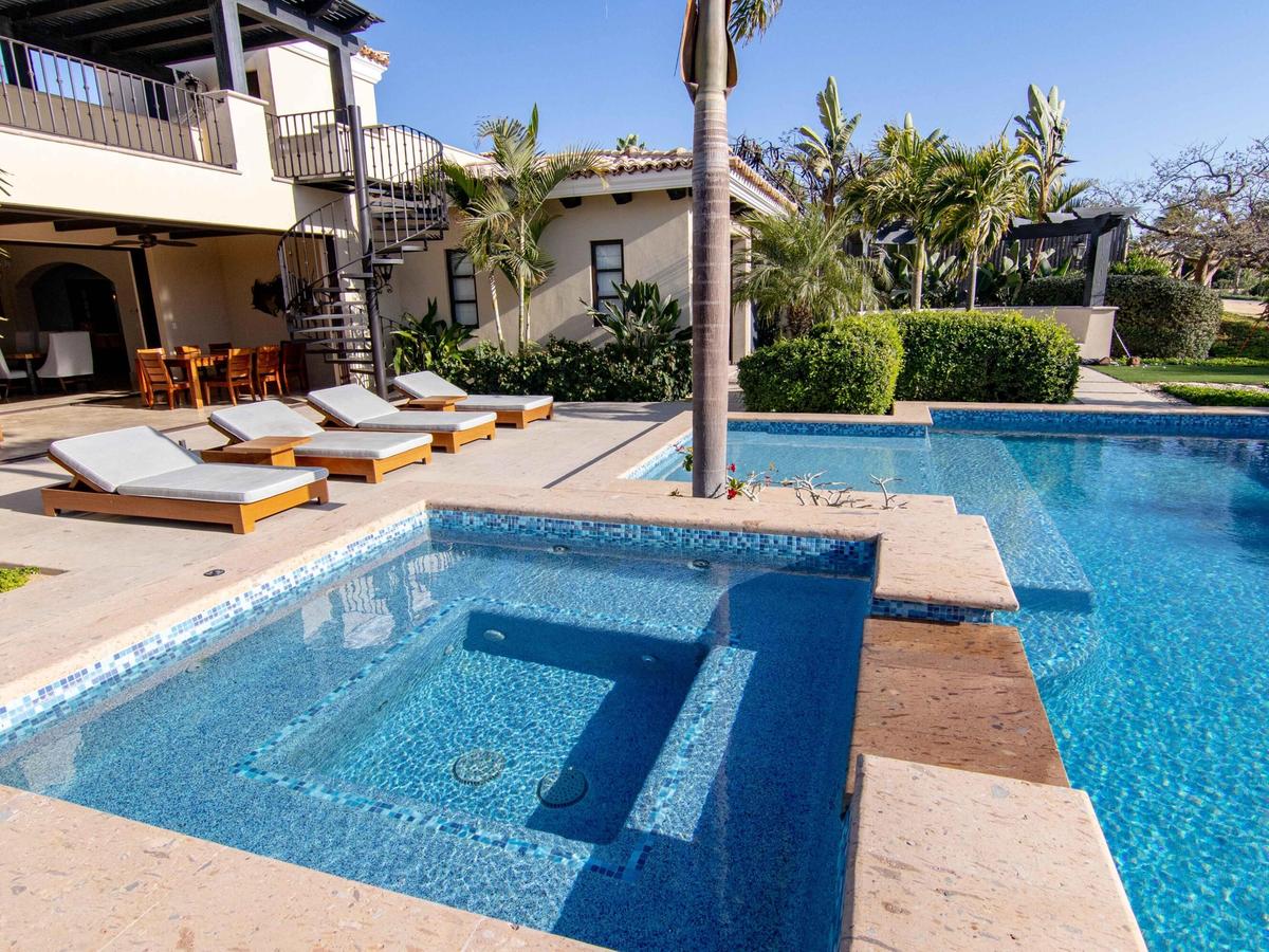 Luxury villa patio with cushioned loungers, a private hot tub and pool, tropical landscaping, and an outdoor spiral staircase leading to an upper terrace.