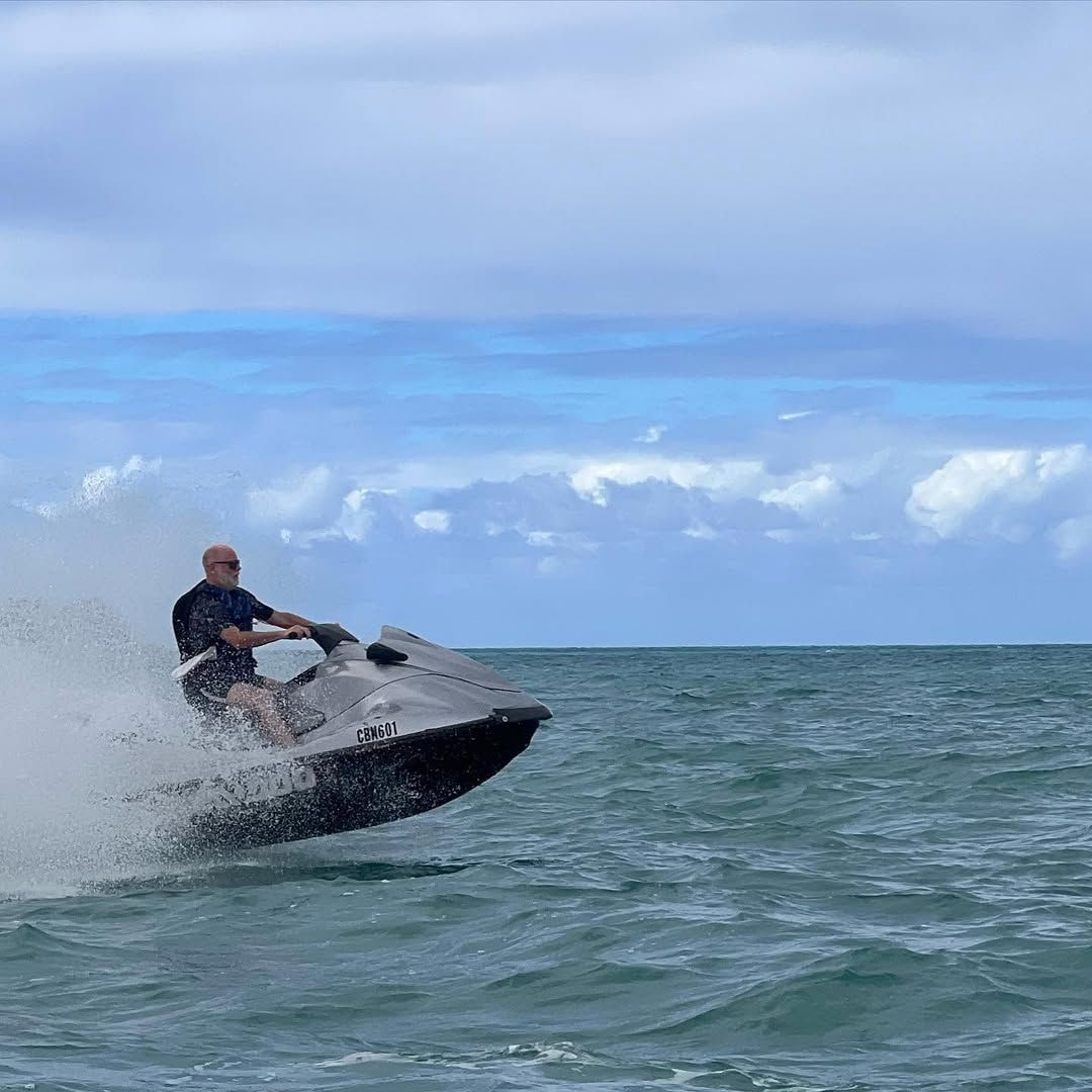 A man rides a jet ski across turquoise waters, catching air as he speeds over the waves. The splash of the sea and clear horizon create an action-packed moment that captures the thrill of adventure in the Bahamas.