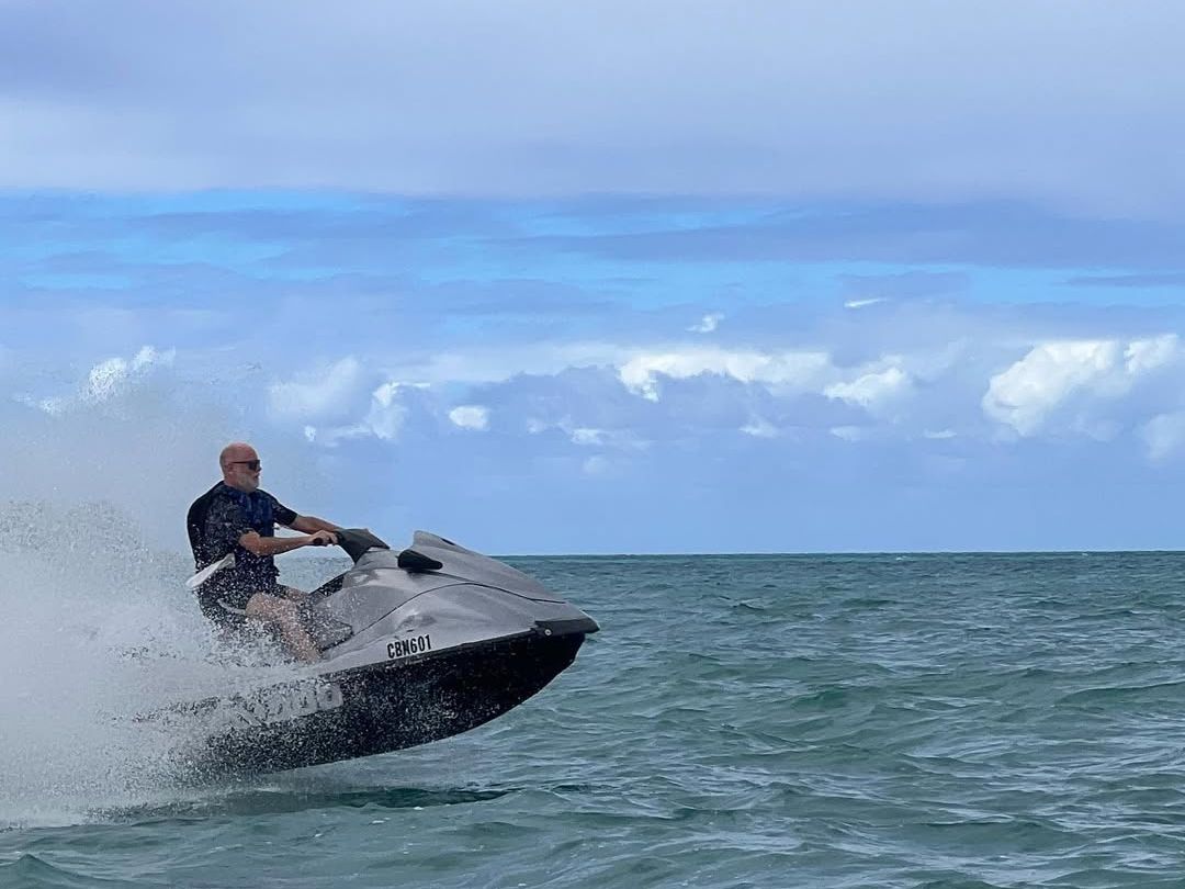 A man rides a jet ski across turquoise waters, catching air as he speeds over the waves. The splash of the sea and clear horizon create an action-packed moment that captures the thrill of adventure in the Bahamas.