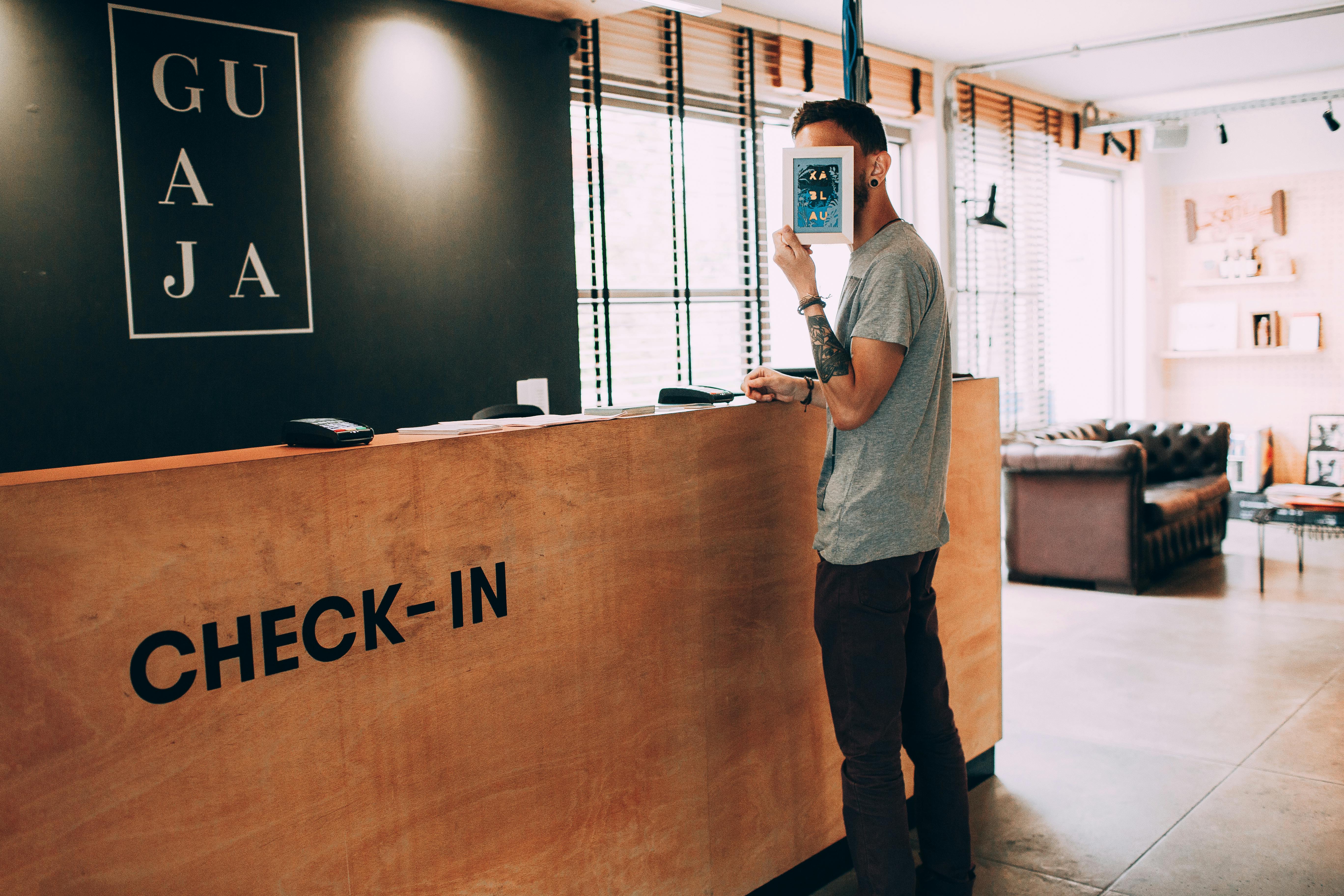 A stylish guest stands at a boutique hotel reception desk during check-in, holding a tablet in front of their face. The modern design and relaxed vibe highlight the personal, welcoming atmosphere of boutique hotels.