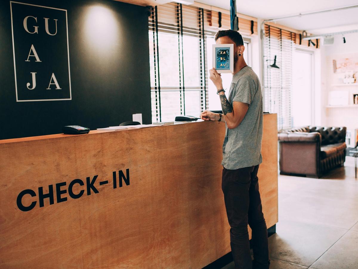 A stylish guest stands at a boutique hotel reception desk during check-in, holding a tablet in front of their face. The modern design and relaxed vibe highlight the personal, welcoming atmosphere of boutique hotels.