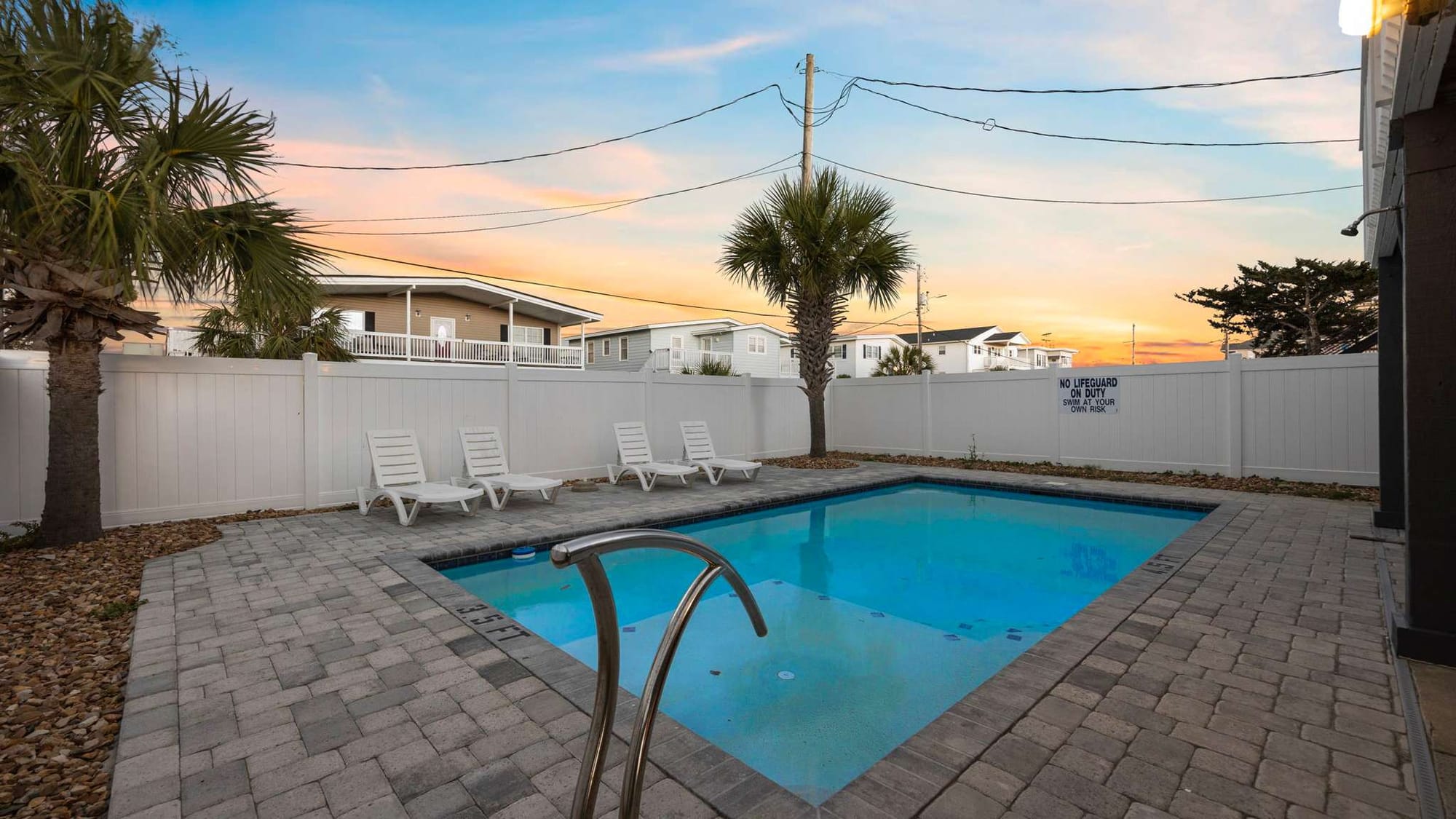 This spacious coastal home features a private pool surrounded by palm trees and lounge chairs, ideal for unwinding after a day at the beach. The warm evening sky adds a golden glow, creating the perfect atmosphere for a laid-back North Myrtle Beach vacation.