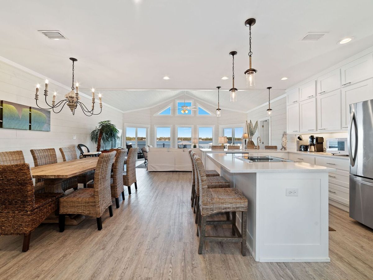 Bright and airy open-concept kitchen and dining space with wicker seating and large windows facing the water. A great option for big families planning a last-minute beach getaway.