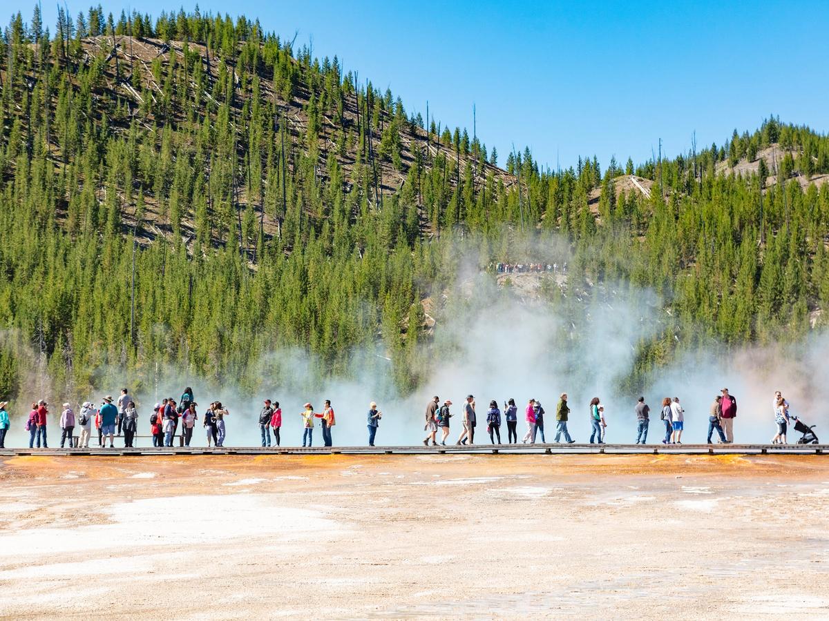 Visitors walk along a boardwalk surrounded by rising steam from geothermal features in Yellowstone National Park. The mix of colorful ground, mist, and pine forests shows why Yellowstone is one of the most unique parks in the U.S. It’s a must-see spot for first-time visitors.