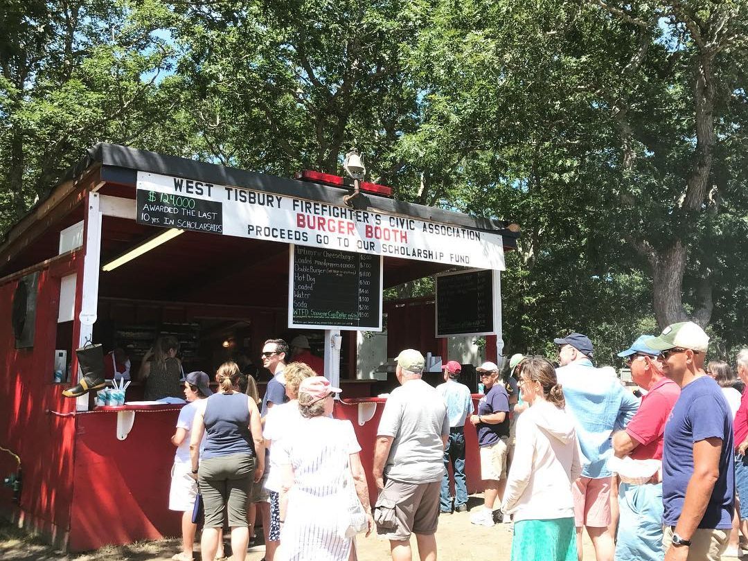 Visitors line up at the West Tisbury Firefighters Civic Association Burger Booth during the Martha’s Vineyard Agricultural Fair. The summer sun, friendly chatter, and the smell of grilled food create a classic fairground experience for locals and visitors alike.