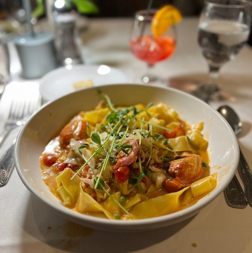 A rustic table filled with colorful dishes including seafood paella, mussels, and fresh appetizers. The variety of plates creates a warm and inviting dining scene perfect for sharing with friends. Restaurants like Old Yarmouth Inn are known for generous portions and classic coastal flavors.