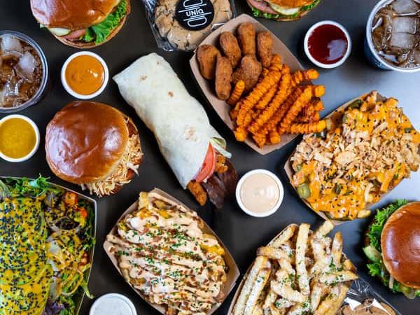 A colorful spread of burgers, fries, loaded nachos, and wraps from UNiQ Burger, paired with sauces and drinks. The bold presentation makes this comfort food spot perfect for anyone craving variety and flavor.