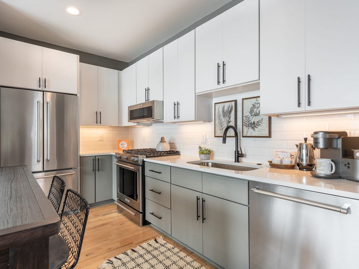 A sleek modern kitchen with stainless steel appliances, white cabinetry, subway tile backsplash, and a cozy coffee station on the counter.