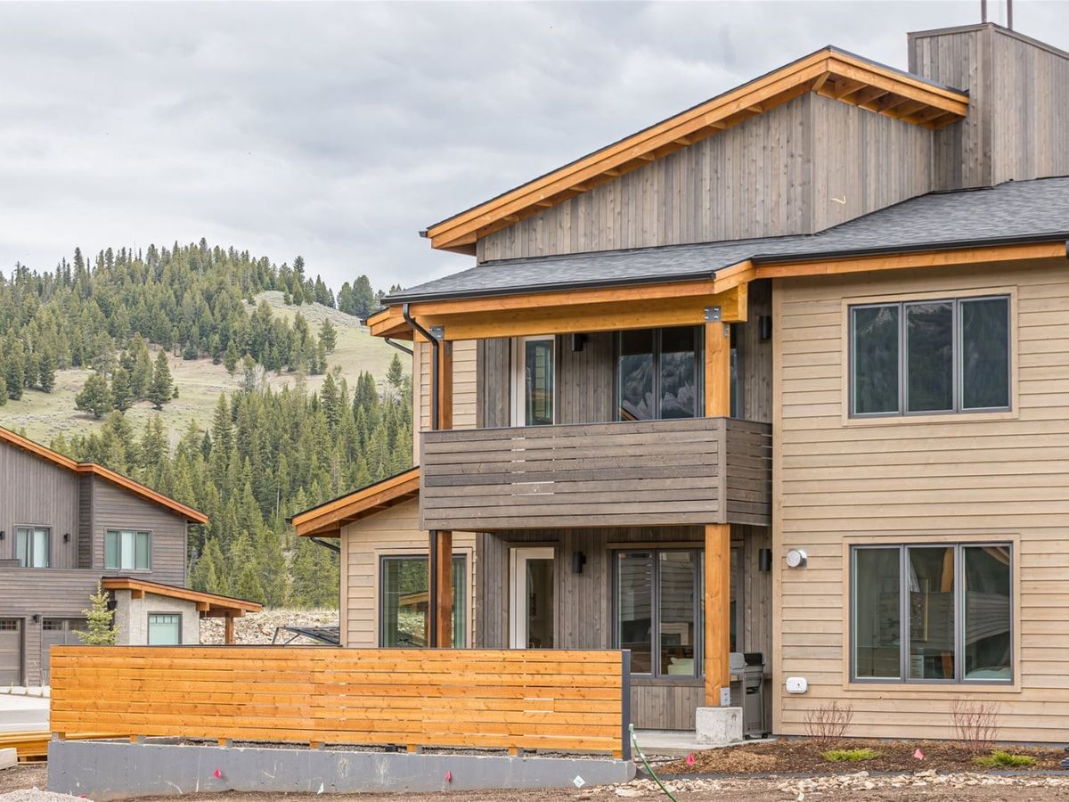 A modern mountain townhome with wood siding and clean lines sits beneath forested hills. This home blends comfort and convenience for families or groups looking to stay close to adventure in Big Sky.