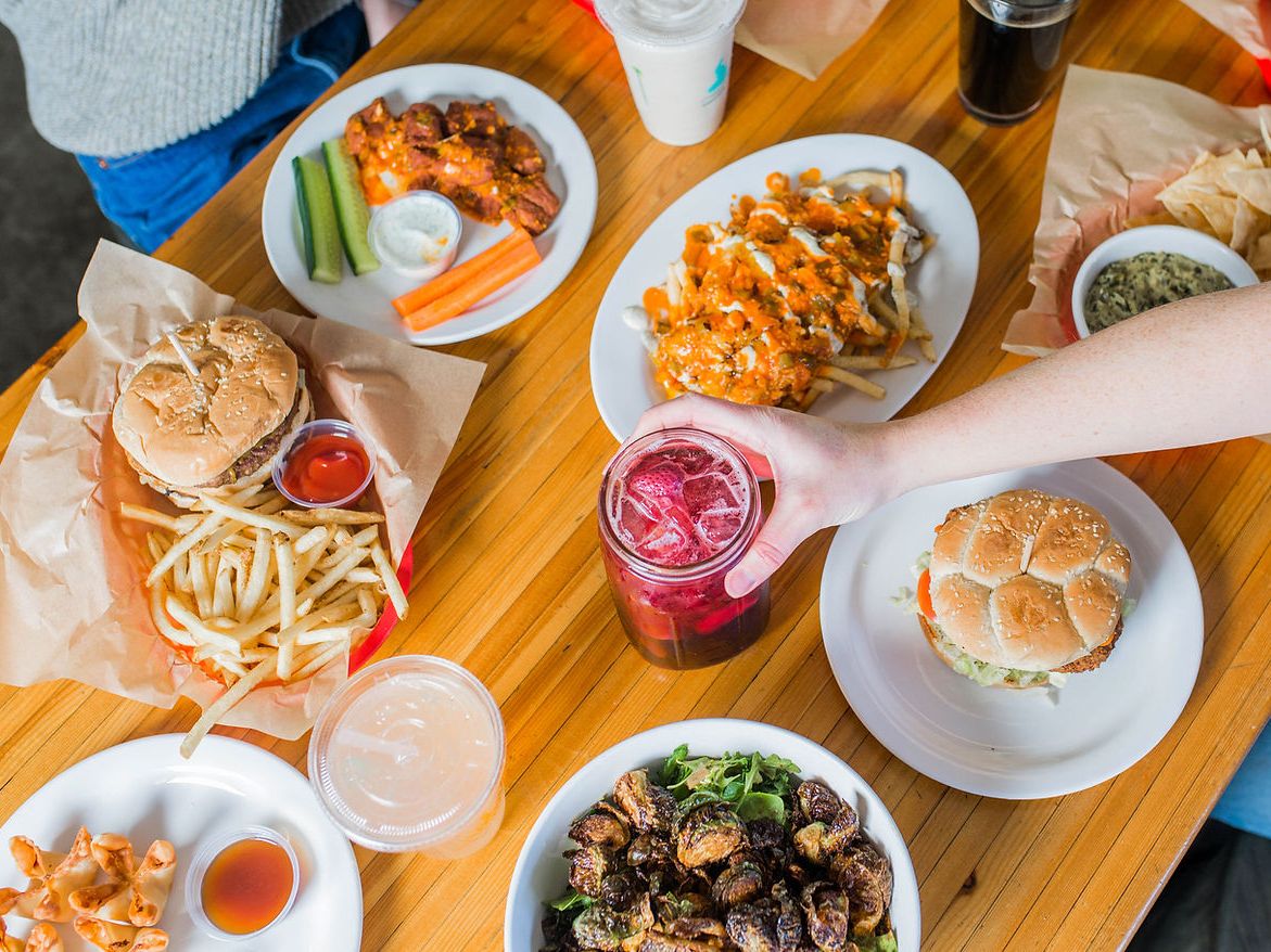 A casual dining spread with burgers, fries, wings, salads, and colorful drinks at Green New American. The mix of comfort food and healthier sides makes it a local favorite.