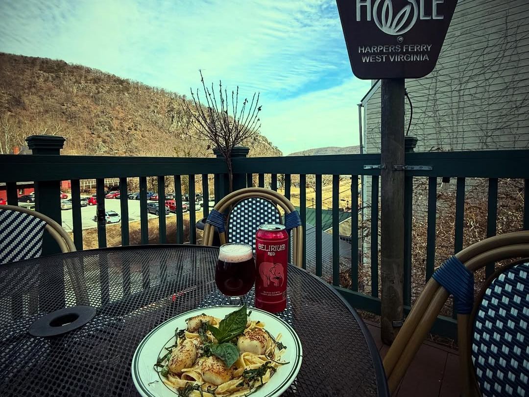A plate of scallop pasta with fresh herbs is served alongside a craft beer on the patio of The Rabbit Hole Gastropub. Mountain views in Harpers Ferry add to the cozy, local dining vibe.
