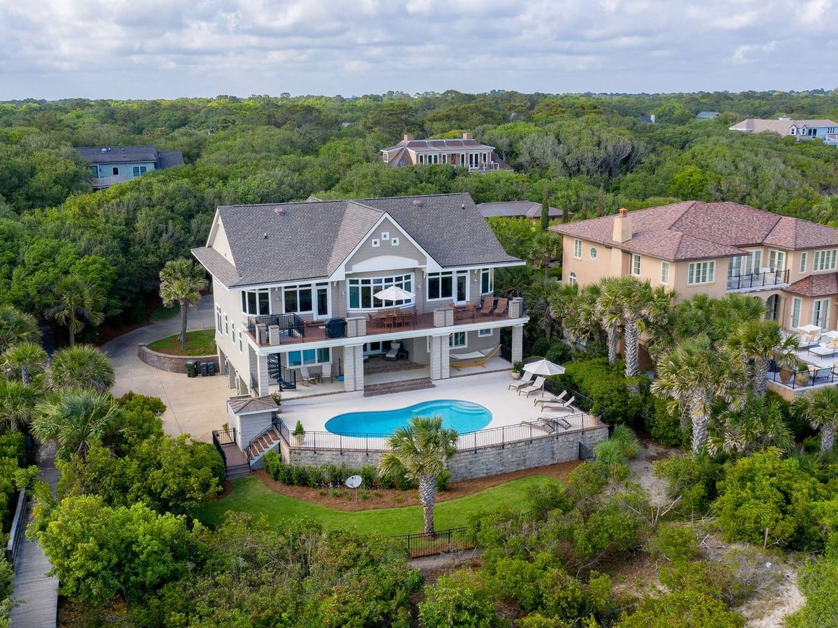 Spacious coastal home featuring a large pool deck surrounded by lush greenery. Offers plenty of outdoor space for family gatherings and beachside relaxation.