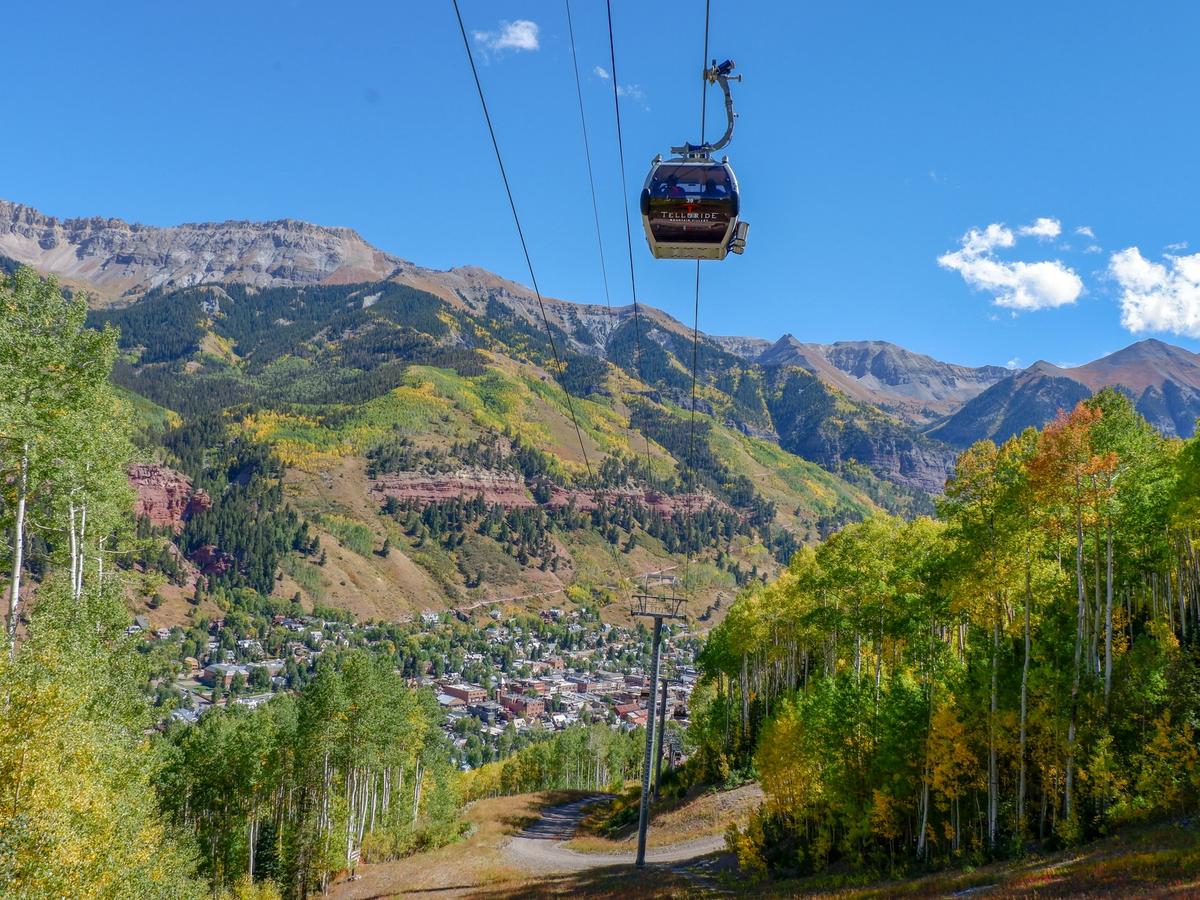 A gondola glides above a golden aspen-lined mountain trail, overlooking the picturesque town of Telluride nestled in the heart of the Rocky Mountains.