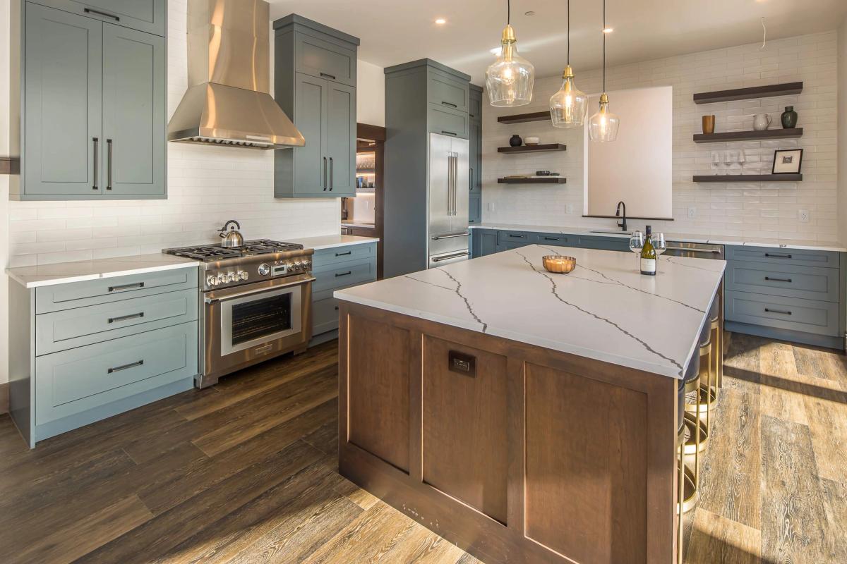 A bright, modern kitchen with a large marble island, soft blue cabinets, and stainless steel appliances. Pendant lights and open shelving add a clean, upscale feel, making this space perfect for cooking and gathering. The design blends mountain cabin charm with modern comfort.