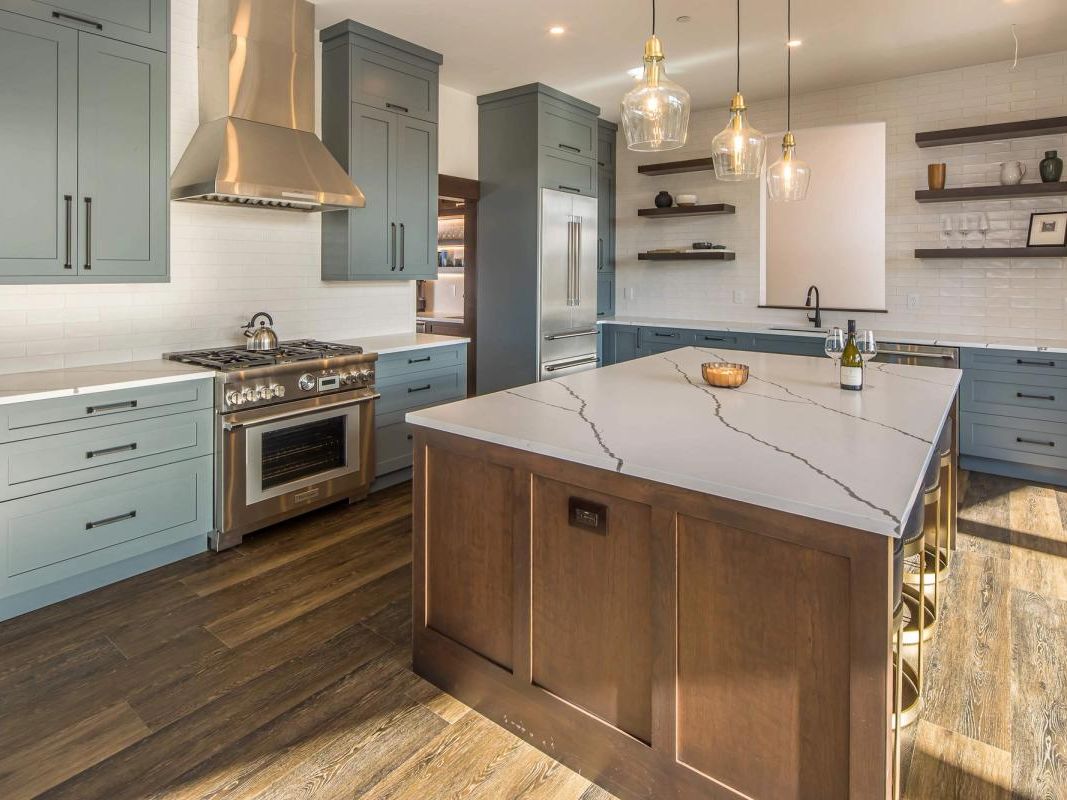 A bright, modern kitchen with a large marble island, soft blue cabinets, and stainless steel appliances. Pendant lights and open shelving add a clean, upscale feel, making this space perfect for cooking and gathering. The design blends mountain cabin charm with modern comfort.