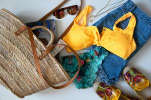 Yellow bikini top, shoes, beach bag, and glasses laid on white ground