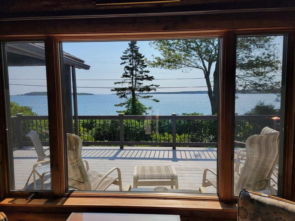 A lakeside deck with comfortable chairs offers wide views of the calm water and nearby trees. Large windows frame the peaceful setting, creating a quiet spot to enjoy morning coffee.