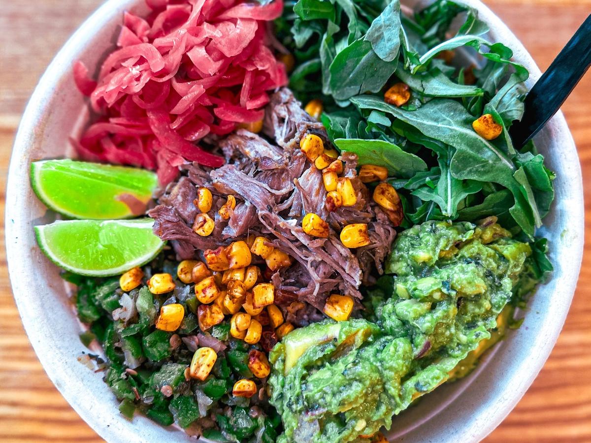 A colorful burrito bowl packed with pulled pork, grilled corn, guacamole, lime, and pickled onions. Every bite bursts with flavor, freshness, and a touch of island flair.