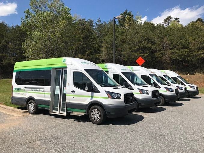 Greenway Public Transit vans line up under a clear sky, ready to shuttle riders across Western North Carolina. This eco-friendly service makes traveling around the mountains simple and stress-free.