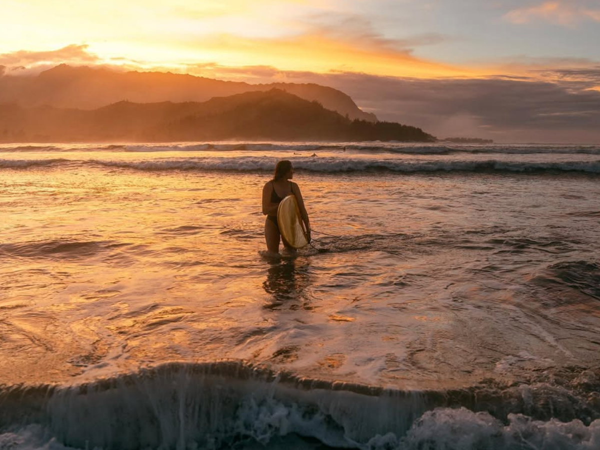 Woman holding surfboard and waves rolling in at Hanalei Beach in Kauai