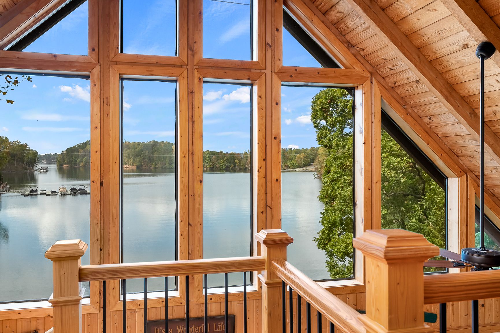 A-frame cabin loft with expansive windows offering a stunning panoramic view of a calm, tree-lined lake.