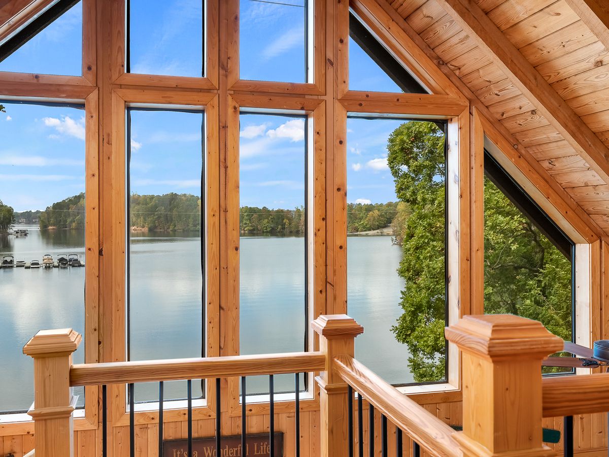 A-frame cabin loft with expansive windows offering a stunning panoramic view of a calm, tree-lined lake.