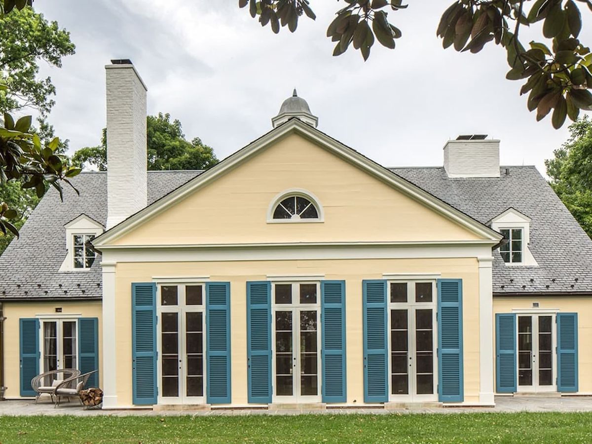 A stately colonial-style home with tall blue shutters, symmetrical windows, and a perfectly trimmed front lawn. Tucked beneath a canopy of trees, this timeless estate offers classic Southern charm and privacy.