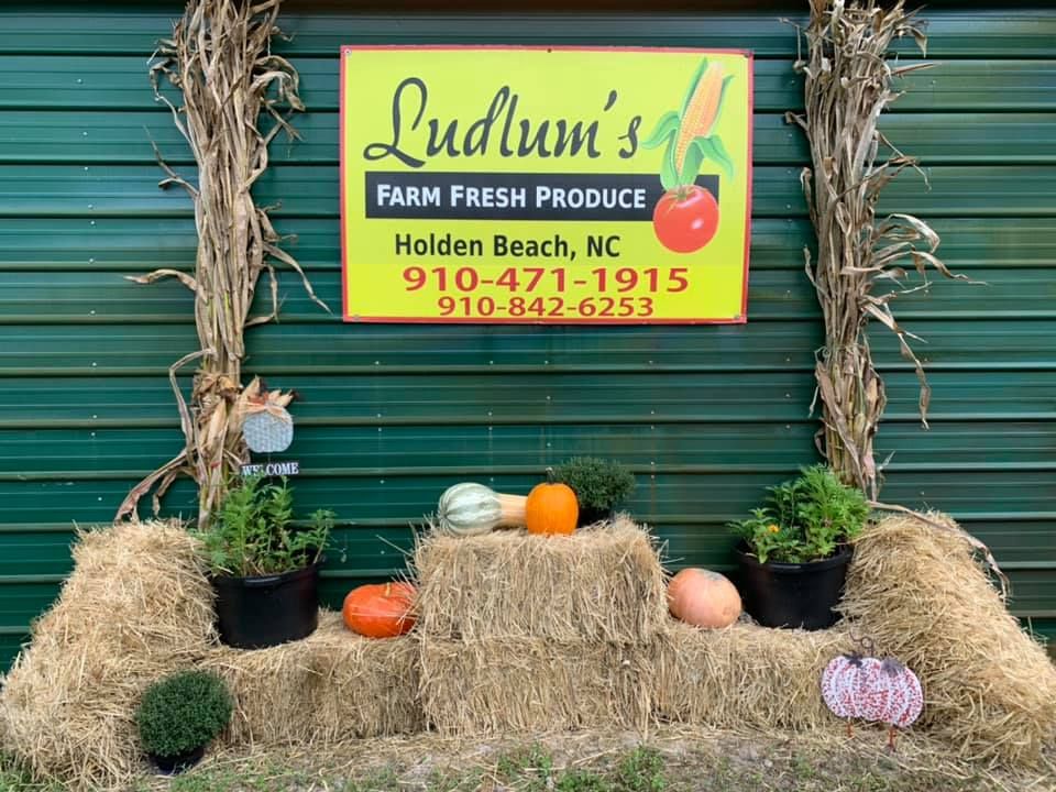 Pumpkins, hay bales, and fall decor sit outside Ludlum’s Produce stand. A cozy local stop in Holden Beach for fresh produce and festive vibes.